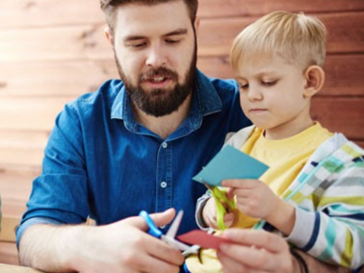 Father cutting paper with his son sitting on his lap.