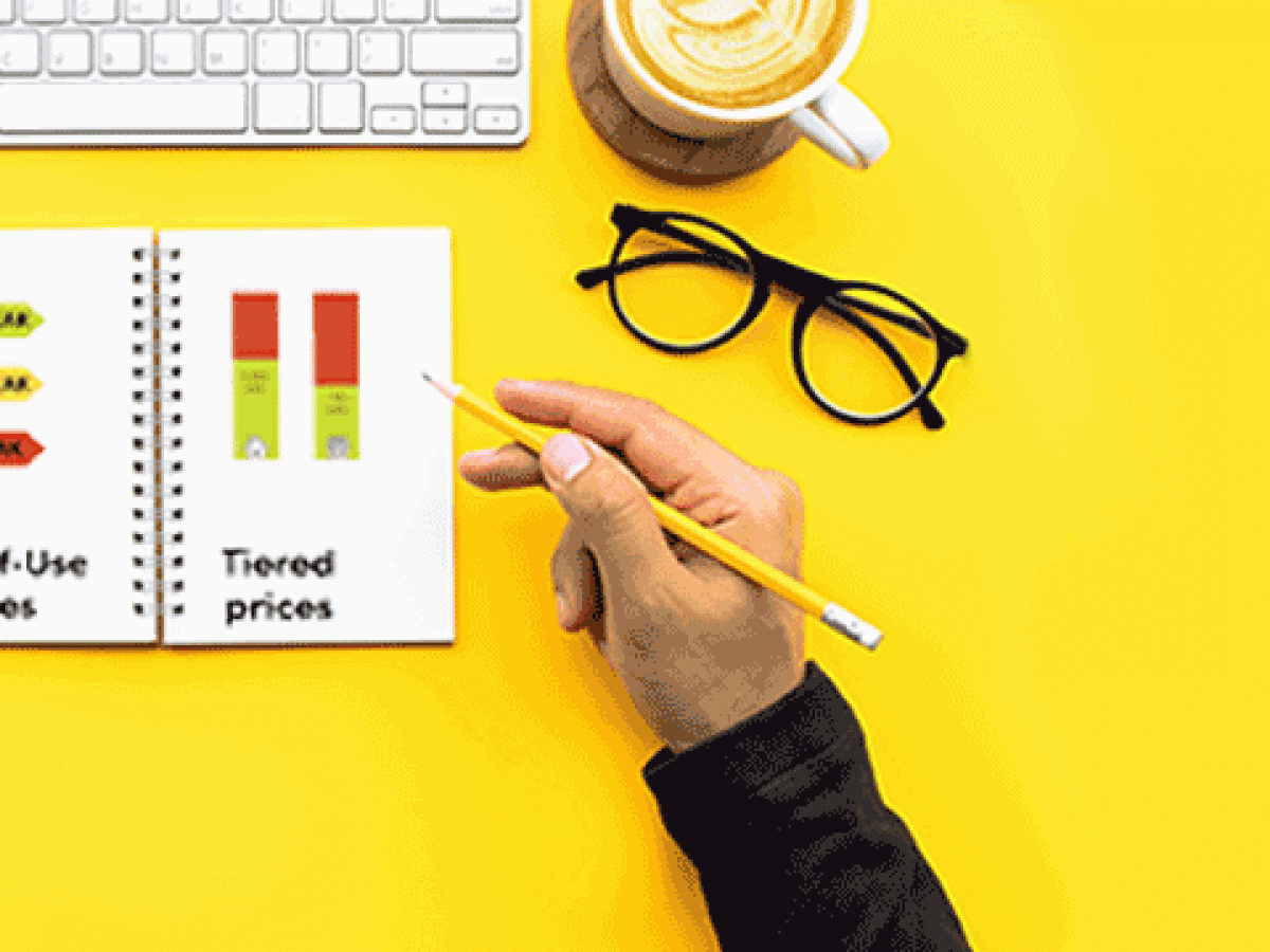 TOU vs Tier? person holding a pencil studying the time of use vs tier graphs. Glasses sitting just above his hands next to a coffee mug and keyboard.