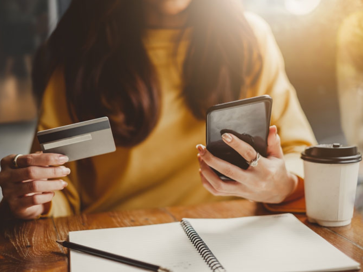 Woman holding a phone in one hand and a credit card in her other about to make an online payment